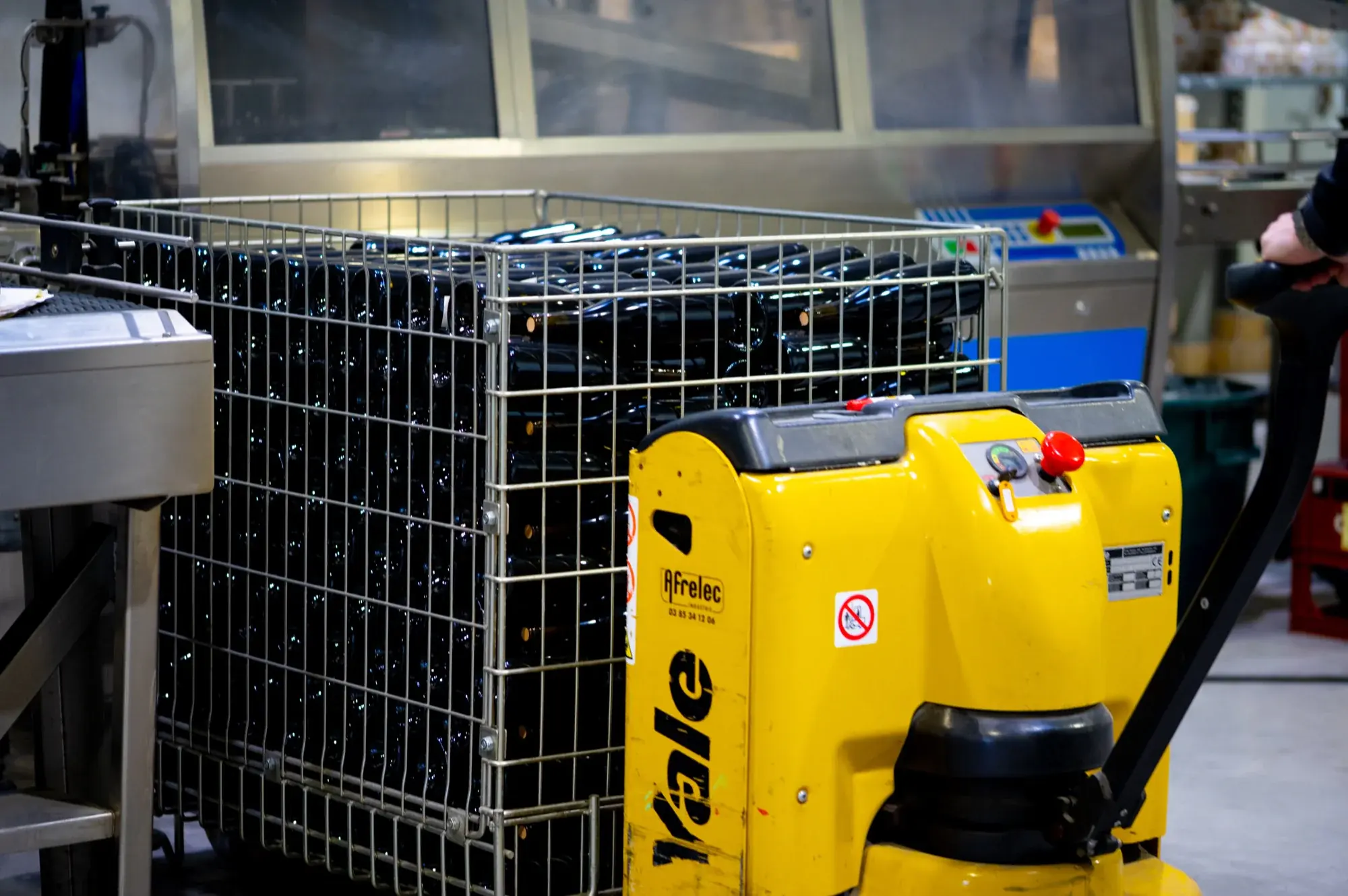Caisse de bouteilles déplacée au transpalette électrique dans l'atelier