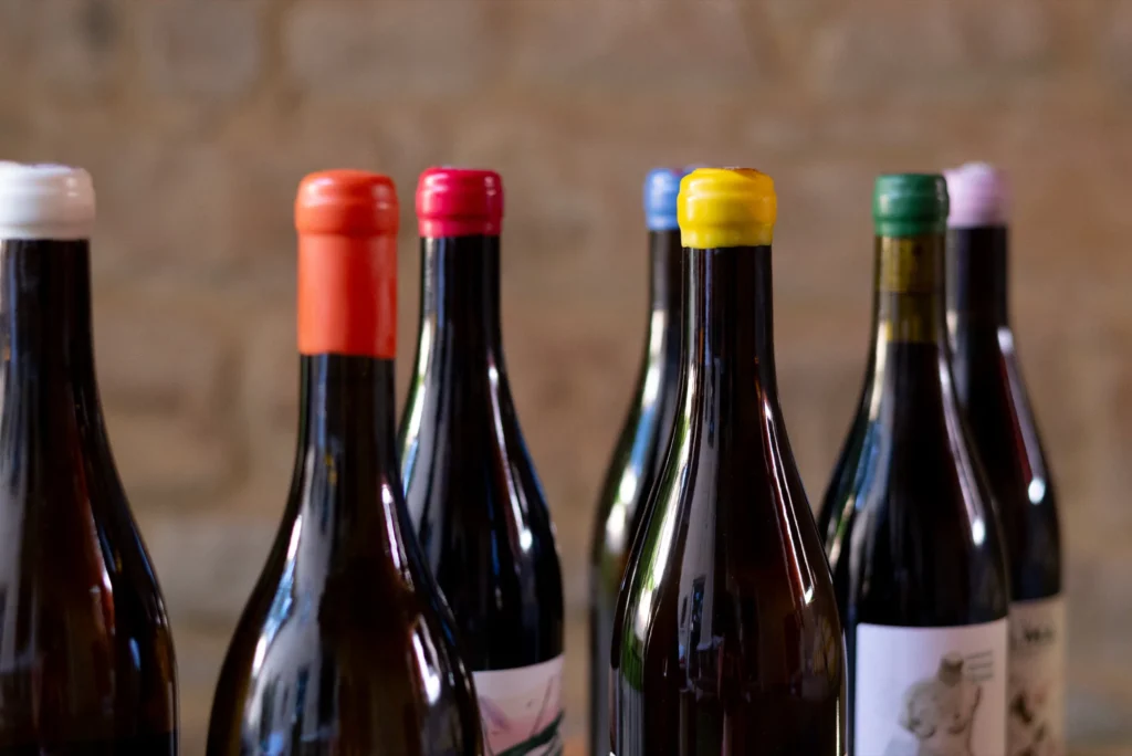 Bouteilles de vin cirées de couleurs variées devant un mur en pierre